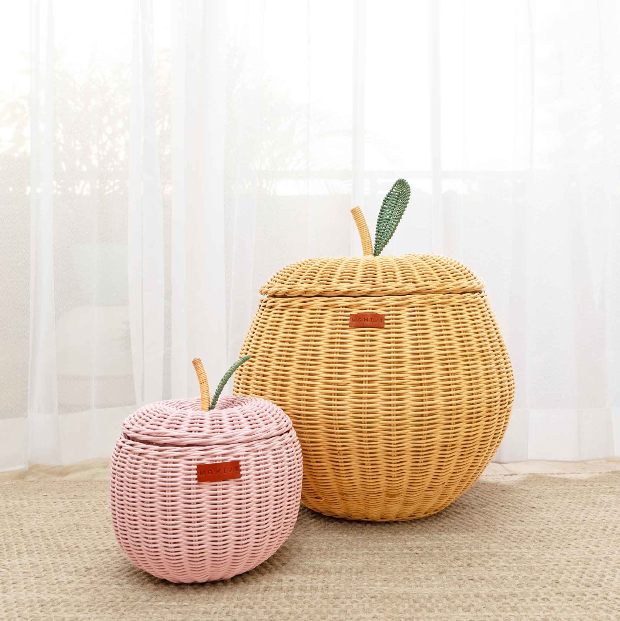 A front view of a small sized pink apple rattan storage basket next to a medium sized natural apple rattan storage basket by MOMIJI.