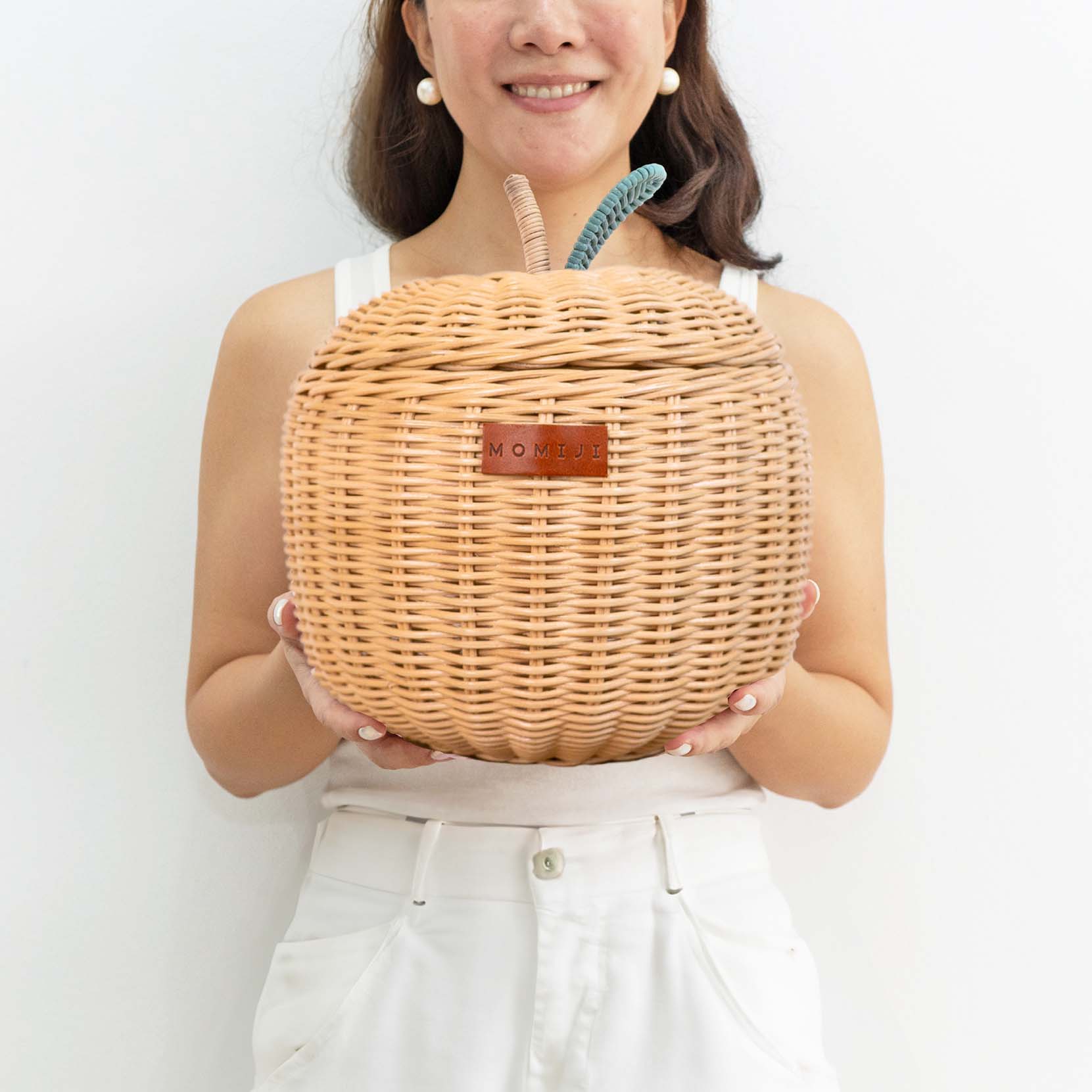 Woman holding a small sized natural apple rattan storage basket by MOMIJI.
