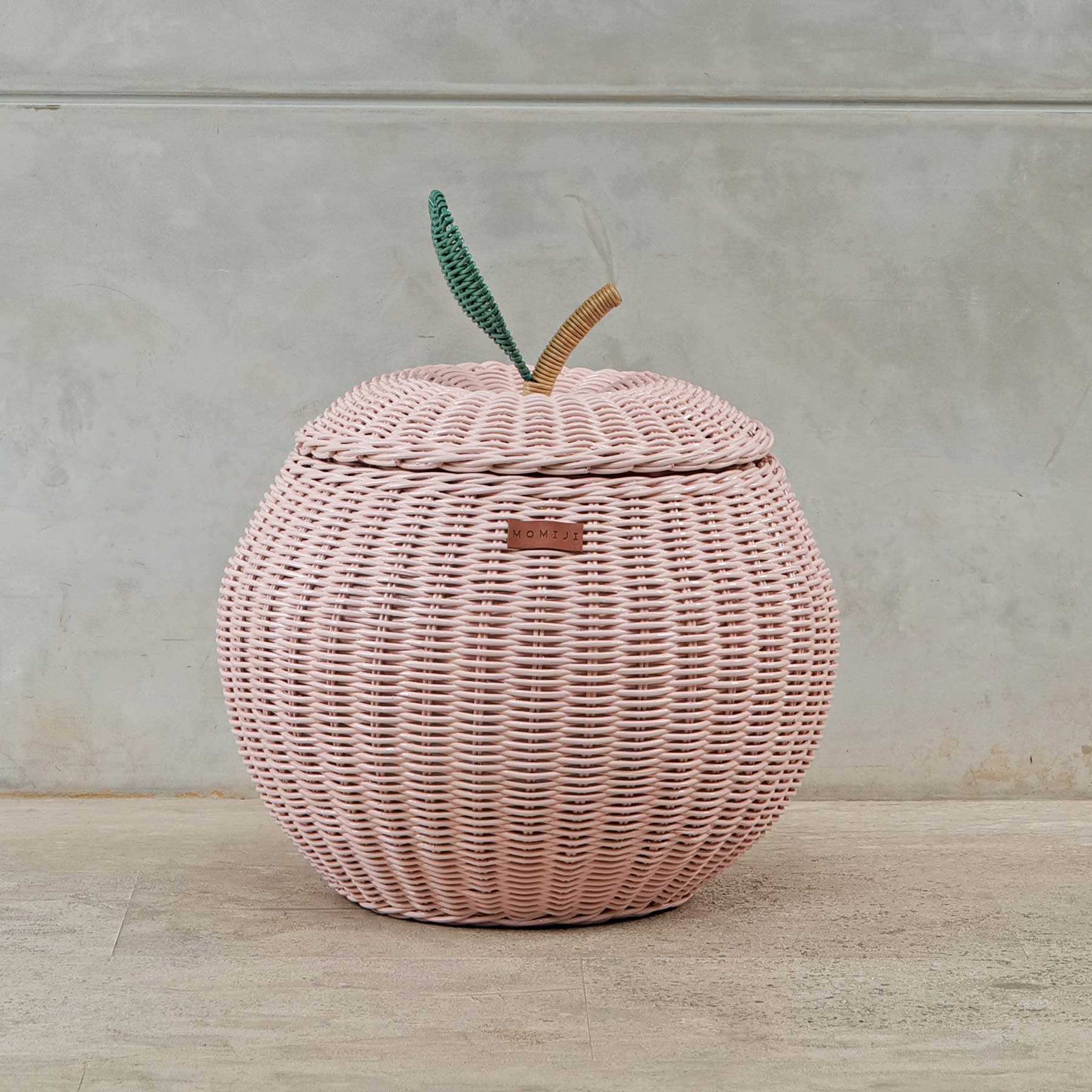Front view of a handcrafted pink rattan wicker apple storage basket in medium size by MOMIJI, showing the MOMIJI label and lid with green leaf and natural stem.