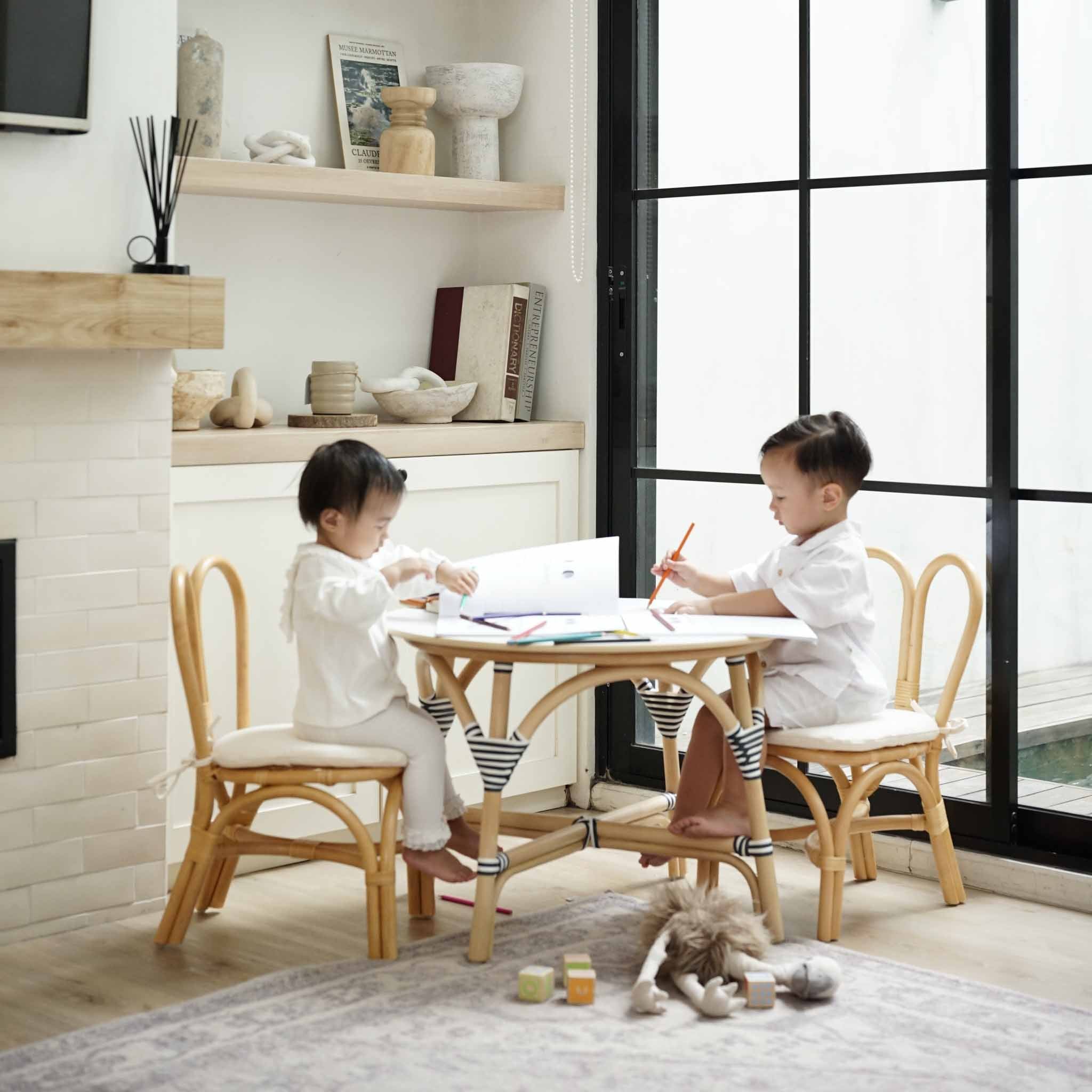 Two children playing and reading together using a handcrafted rattan wicker Aulia Kids Table (Medium) & Set of 2 Bunny Kids Chairs (Natural) by MOMIJI for kids toom decor.