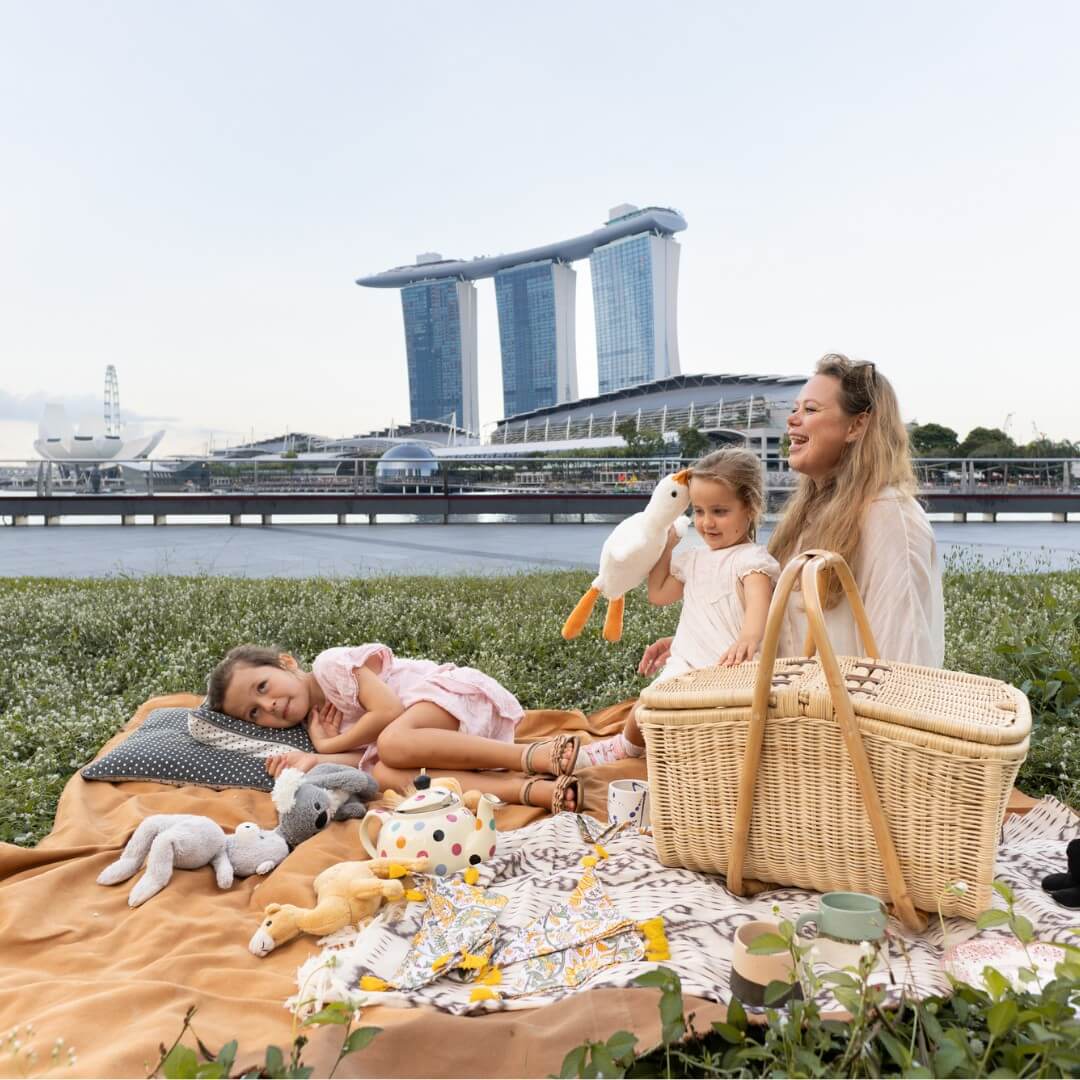 Woman and child sitting on a blanket with toys near an Aurelie rattan picnic basket by MOMIJI, Marina Bay Sands in the background.
