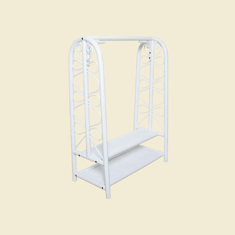 Angled view of the handcrafted white rattan Belle Kids Montessori Clothing Rack by MOMIJI, showcasing its decorative side scrollwork, two storage shelves, and easy-to-assemble design.