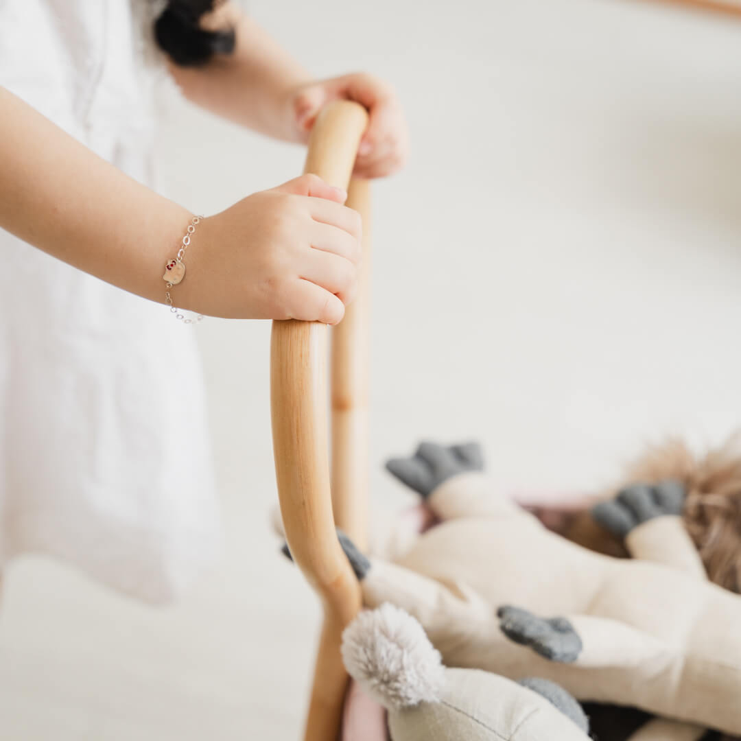Close-up of a child’s hand holding the handle of the handcrafted rattan wicker Colette Doll Stroller by MOMIJI.