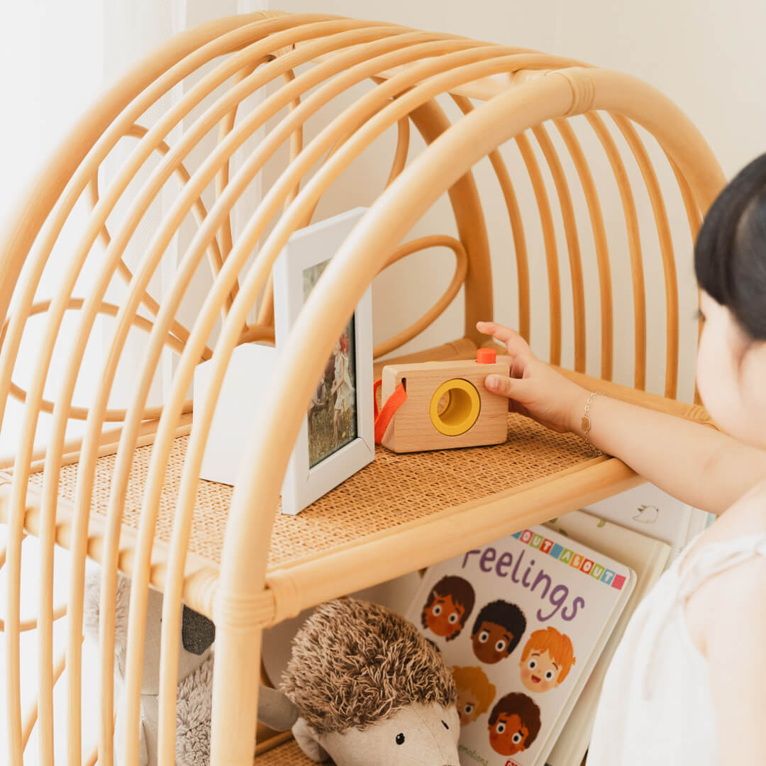Close-up of a child placing a toy camera into the upper storage section of the Daisy Arch Shelf by MOMIJI.
