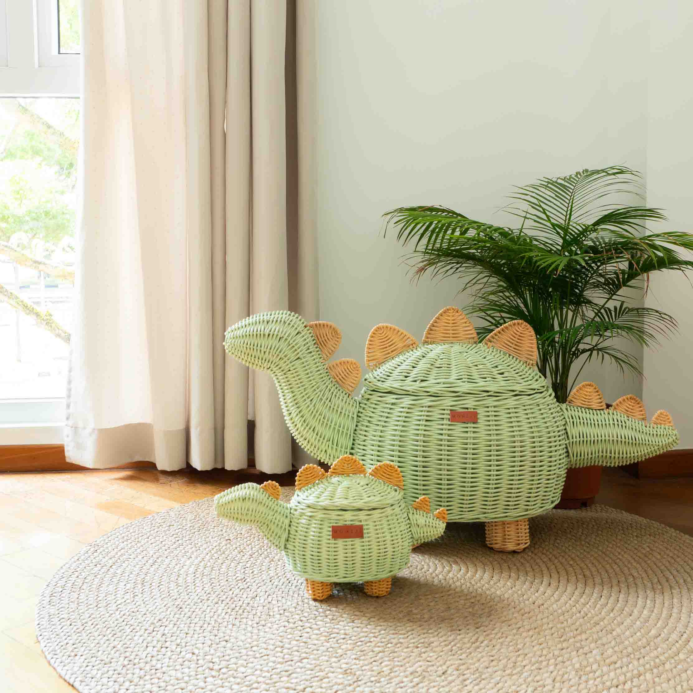 Two mint green Dinosaur Rattan Storage Basket by MOMIJI on a rug with a plant and window in the background.