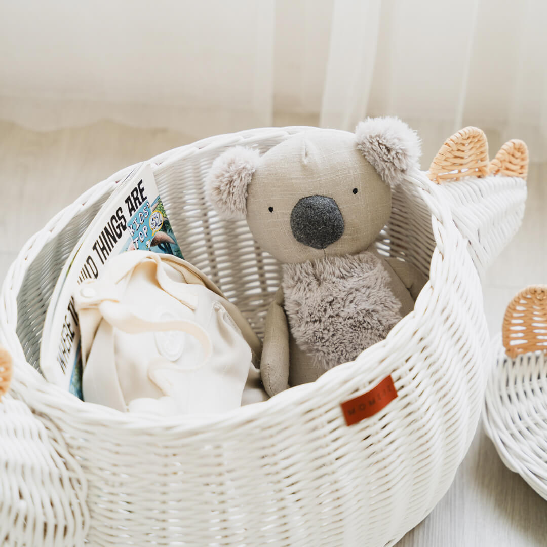 Close up shot inside the white dinosaur rattan storage basket by MOMIJI with a book, a stuffed toy, and a mini bag inside it.