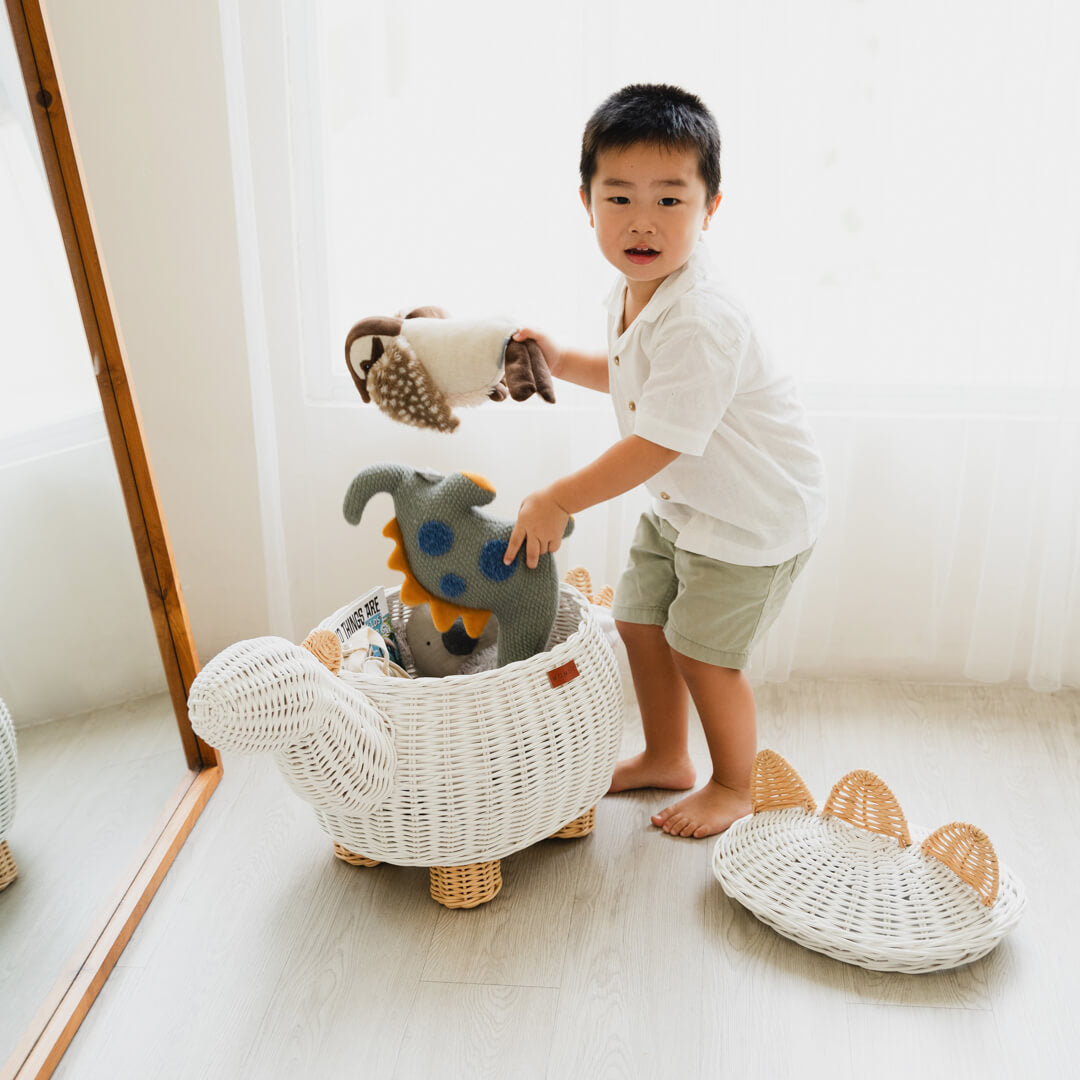 A child cleaning and storing stuffed toys inside white dinosaur rattan storage basket by MOMIJI.