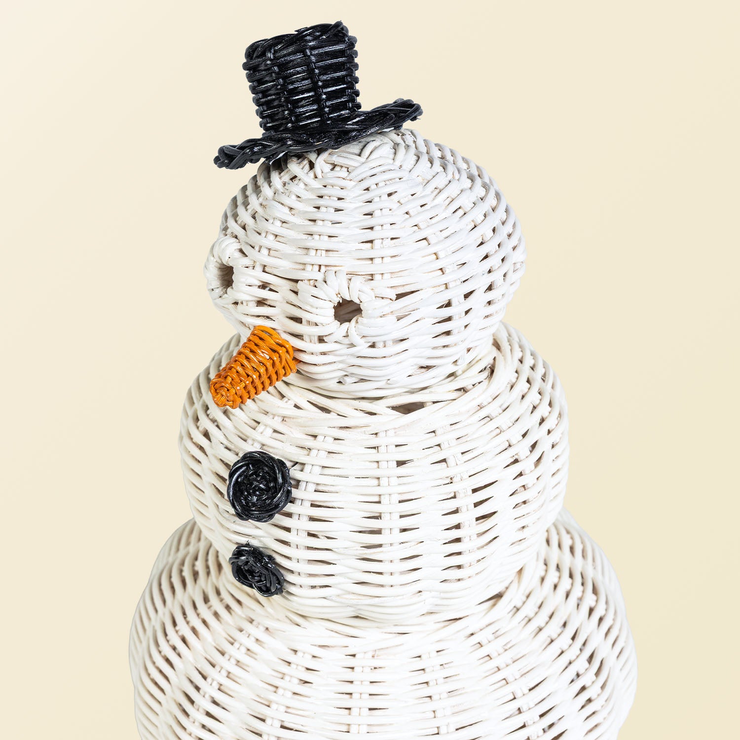 Close-up of a handcrafted rattan wicker snowman basket by MOMIJI showing the round eyes, black top hat, and black round button details.