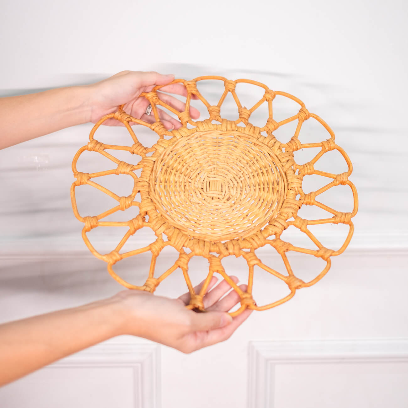 Top view of a hand holding the Floral rattan placemat by MOMIJI, showing its flower-inspired design.
