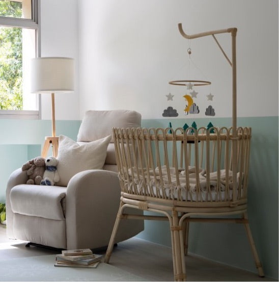 Gerhana Bassinet by MOMIJI placed beside a sofa with hanging toys in a living room.