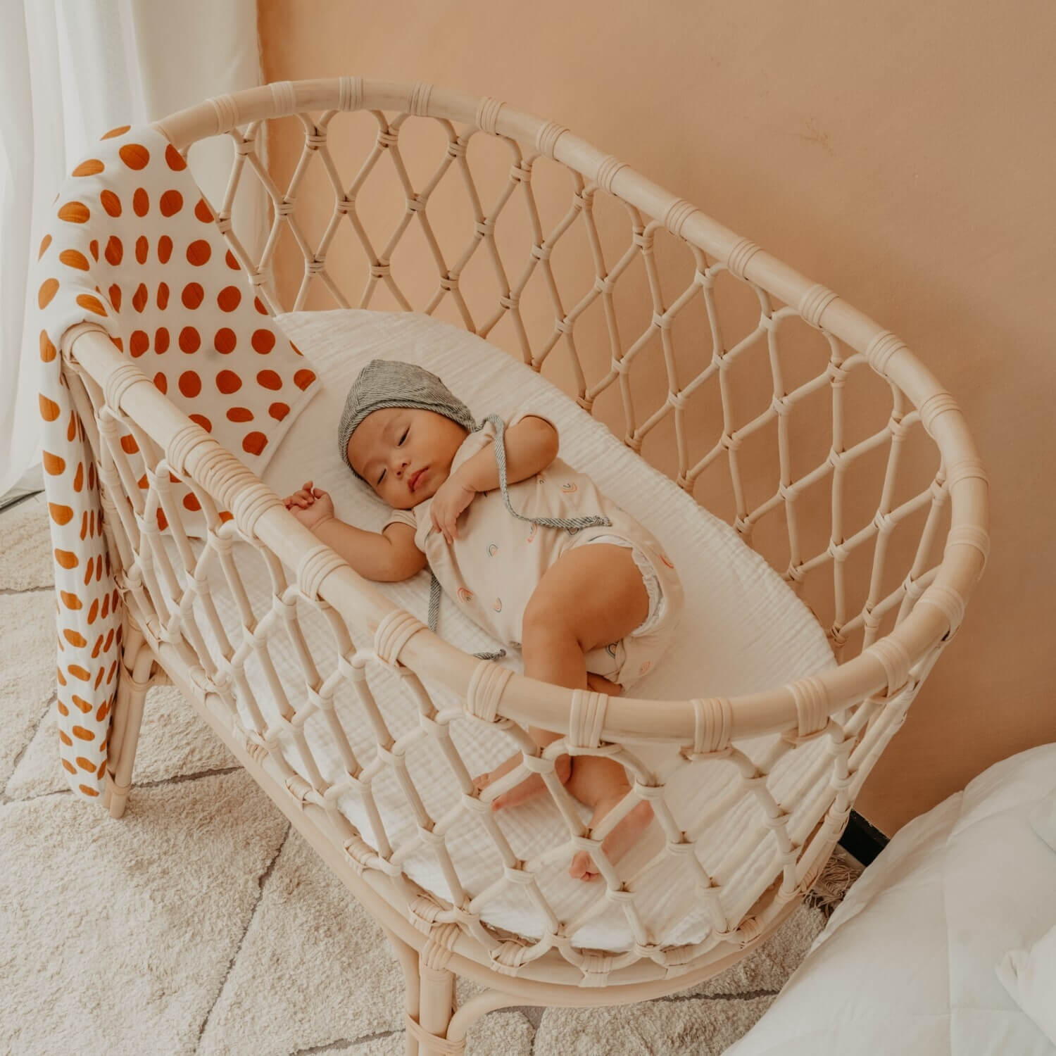 Newborn sleeping in the Layla Bassinet by MOMIJI placed beside a bed in a bedroom.
