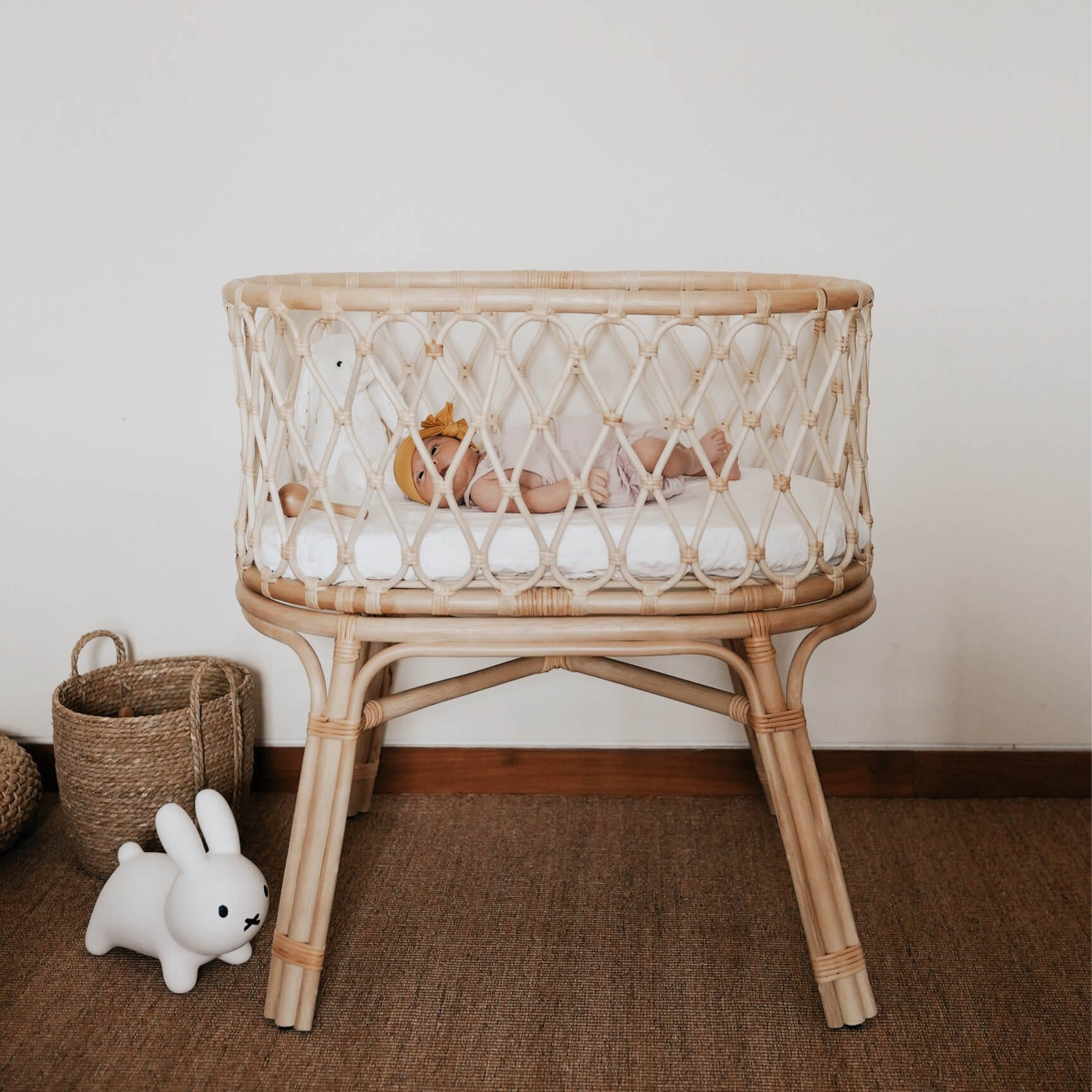 Side view of the Layla Bassinet by MOMIJI with a baby inside, surrounded by toys on a rug.