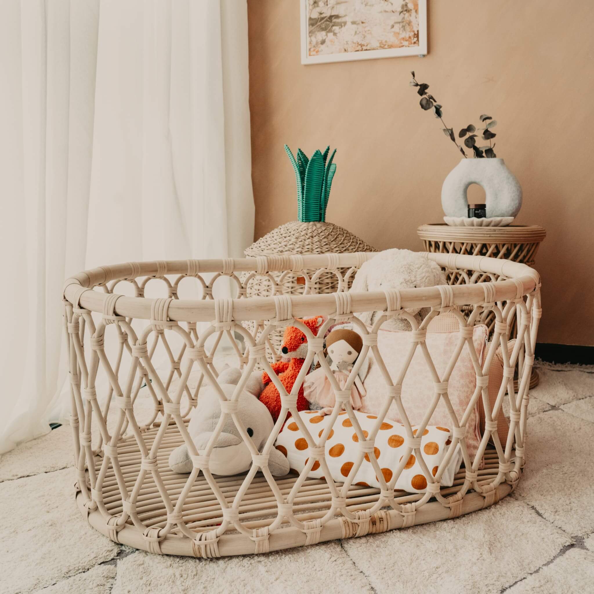 Wicker bassinet styled with plush toys on a wooden floor in a neutral-toned room.