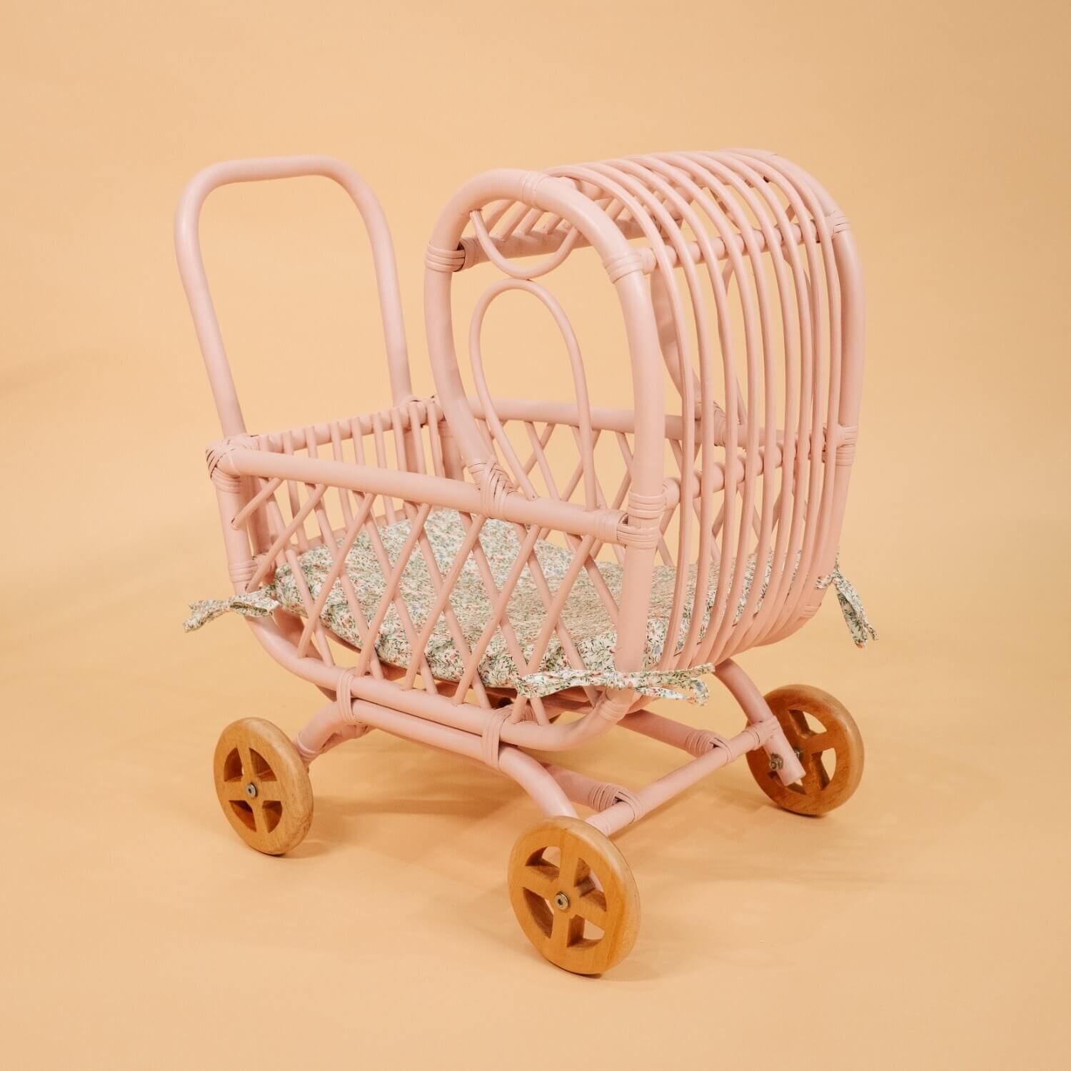 Side view of the handwoven rattan Layla Toy Stroller by MOMIJI in pink with a matching seat pad inside.