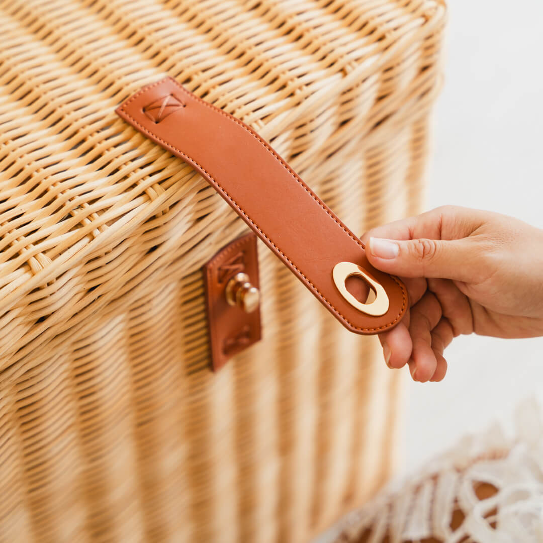 Close-up of a hand opening the front lock on the handcrafted rattan wicker Leon Leather Trunk by MOMIJI.