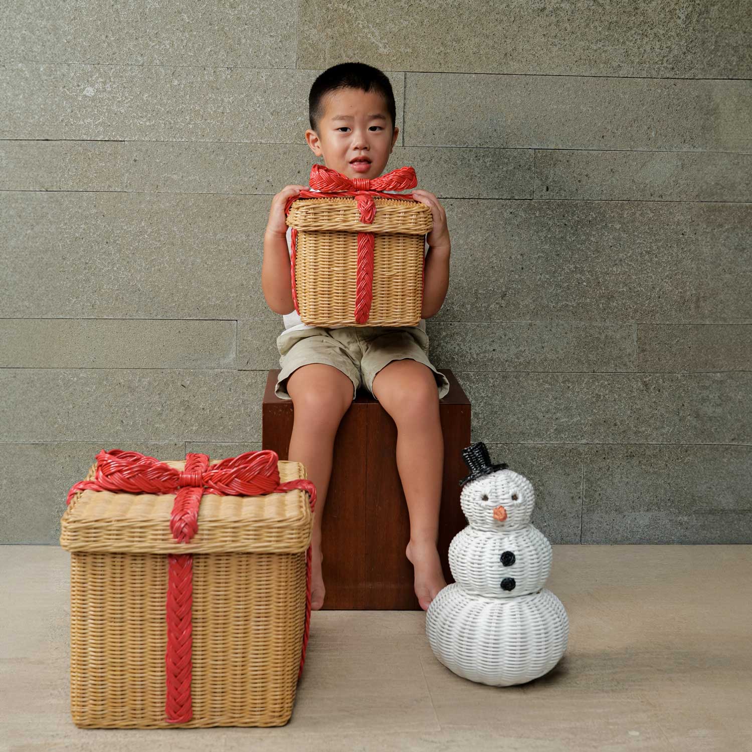 Child Holding a Small Sized Rattan Basket Gift Box with large rattan gift box and snowman rattan basket on the floor.
