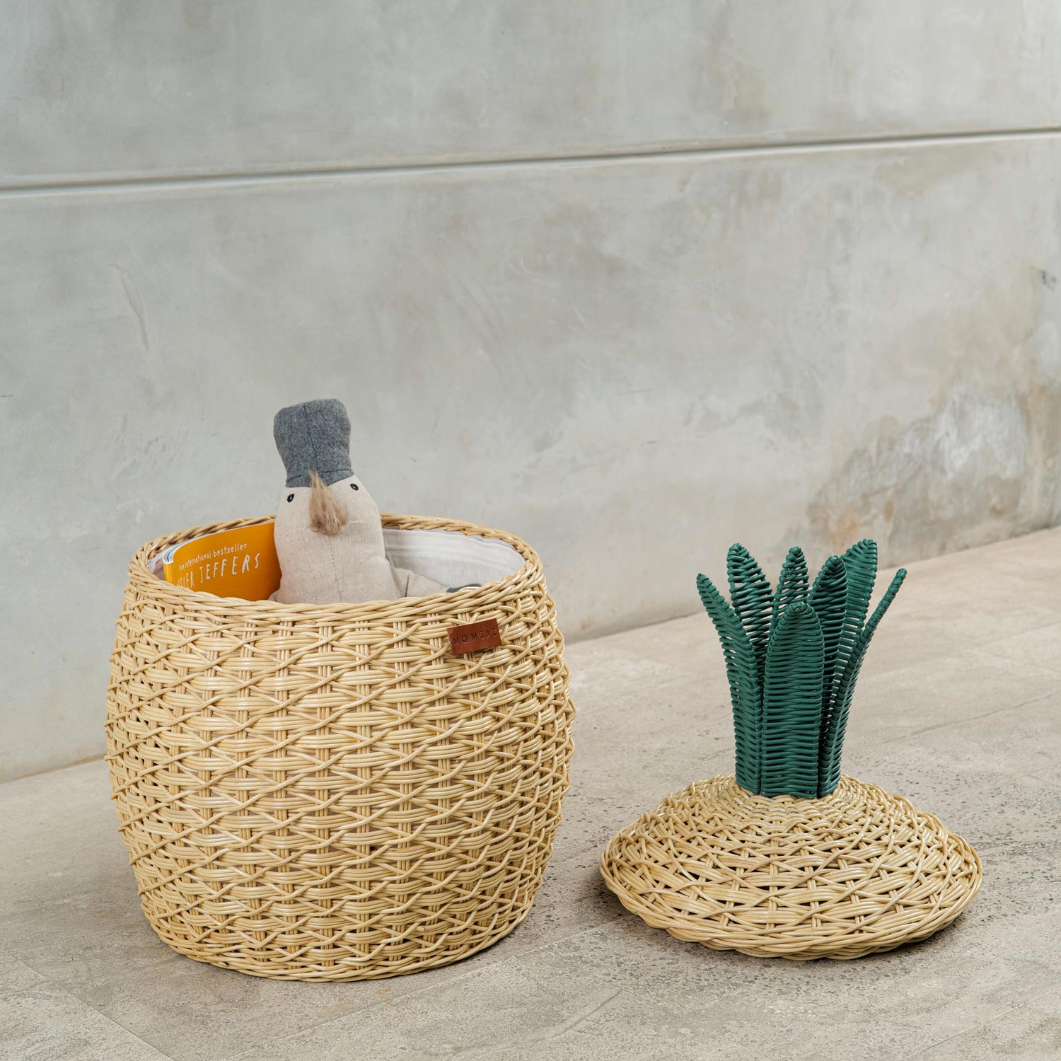 Pineapple Rattan Storage Basket, opened lid on the floor with toys and books Inside.