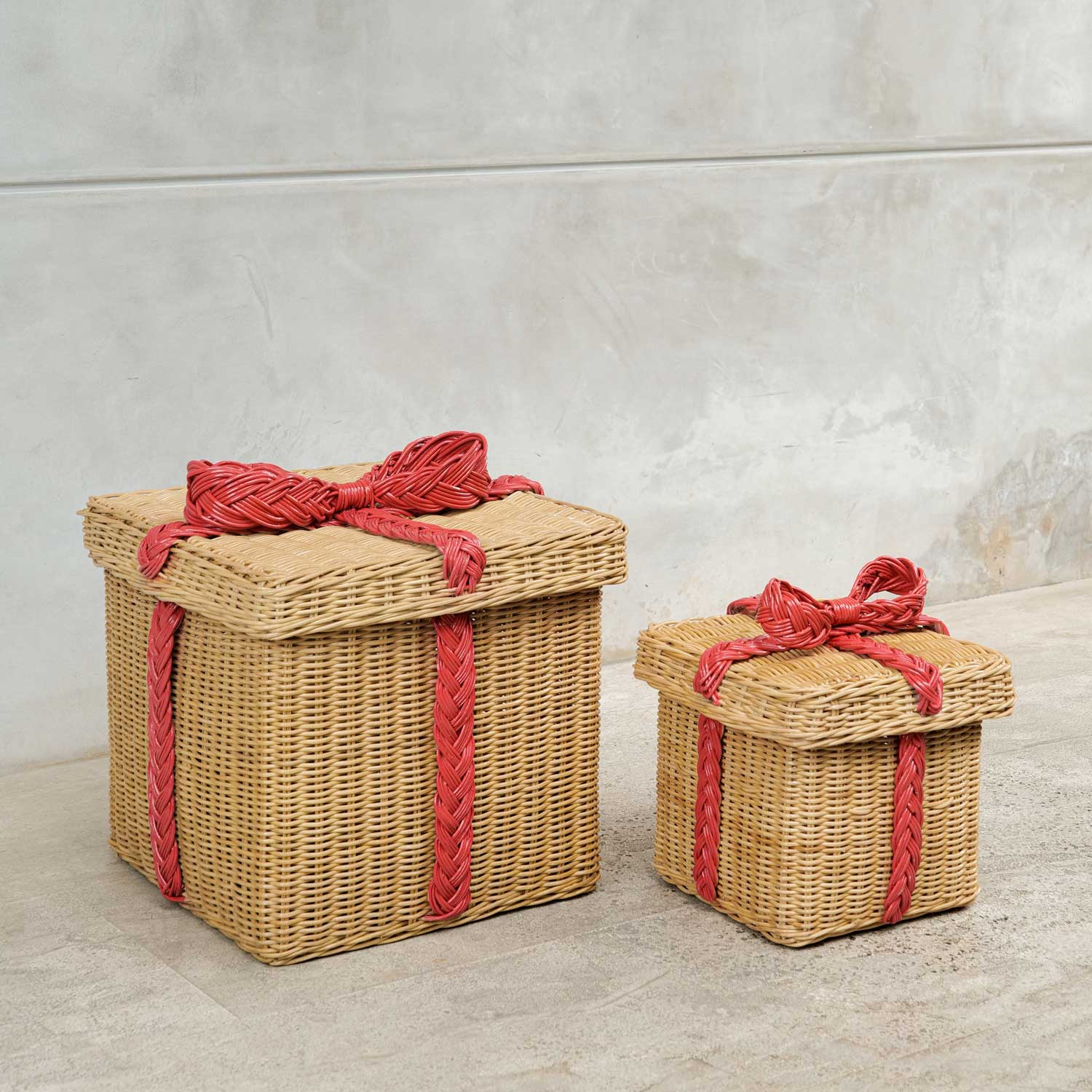 Two Rattan Basket Gift Boxes large and small with red rattan woven ribbons on a concrete surface.
