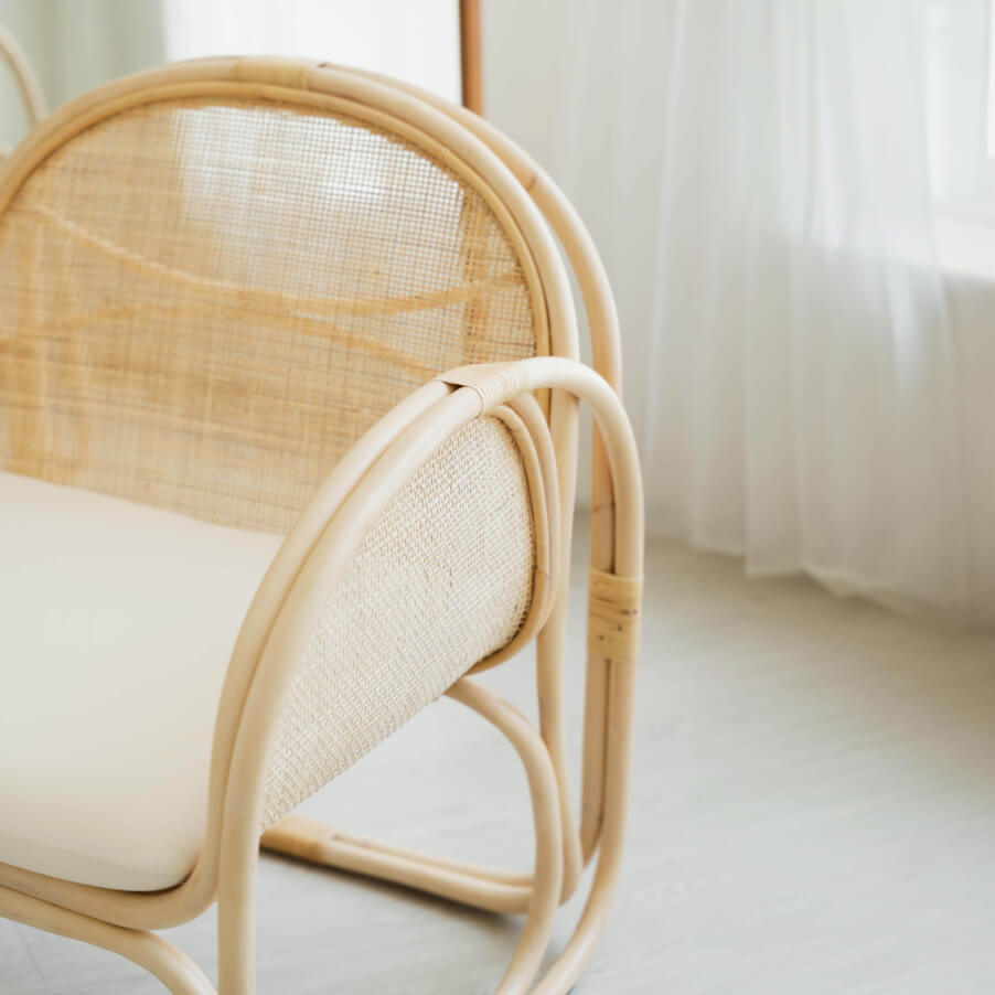 Side close-up of the handcrafted Willow Lounge Chair by MOMIJI in a bright room, emphasizing its curved silhouette and natural rattan texture.