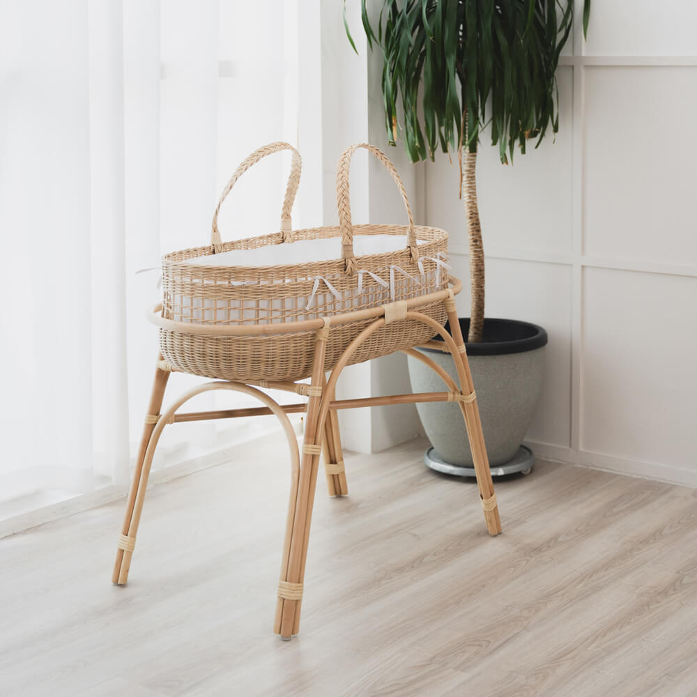 Wicker baby bassinet with fixed stand by MOMIJI in a bright room with a plant and light-colored flooring.