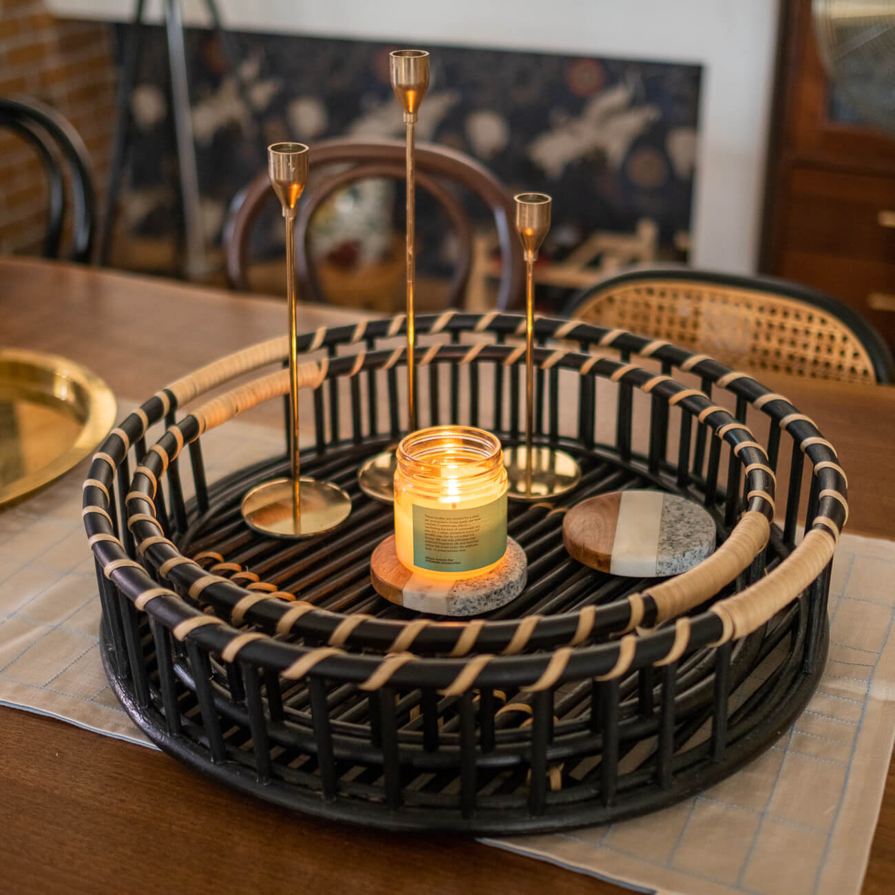 Handcrafted rattan Maru Tray Set by MOMIJI with cutout handles, styled on a table with candles and candle holders.