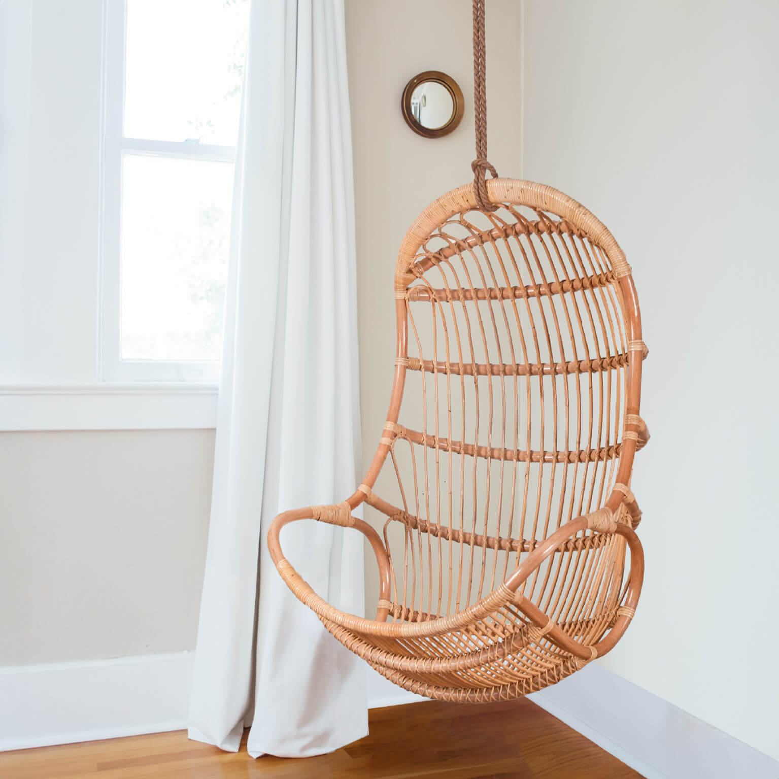 Angled view of the Nest Hanging Chair by MOMIJI hanging outdoors in a natural setting.