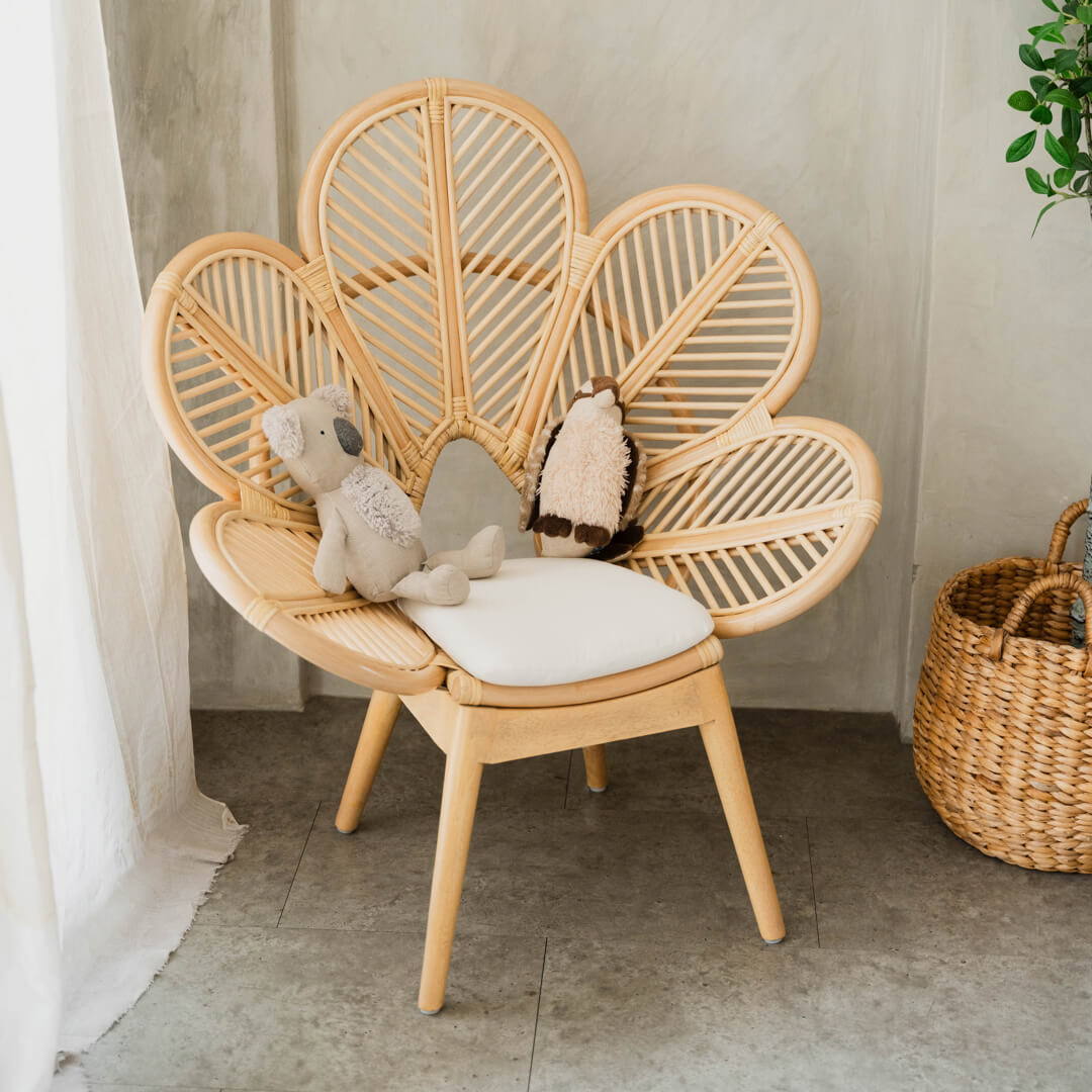Doll seated on the handcrafted rattan Petal Kids Chair by MOMIJI in a room with plants.