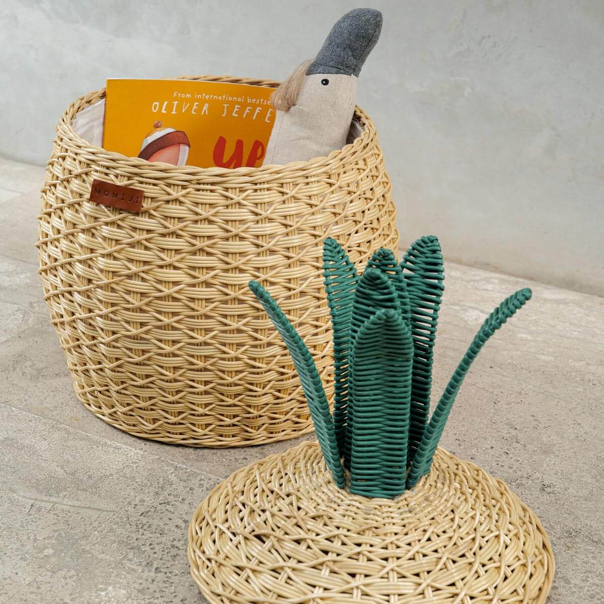 Side view of Pineapple Rattan Storage Basket, opened lid on the floor with toys and books Inside.