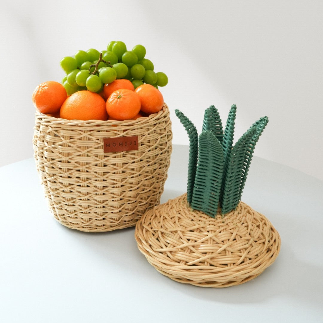 Handcrafted natural pineapple rattan storage basket in small size by MOMIJI shown with the lid off and filled with fruits, highlighting its use as a decorative storage basket.