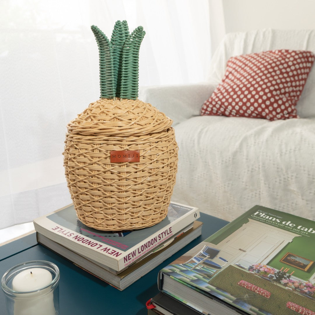 Handcrafted natural Pineapple Rattan Storage Basket in small size by MOMIJI on books with a candle and magazine on a coffee table.