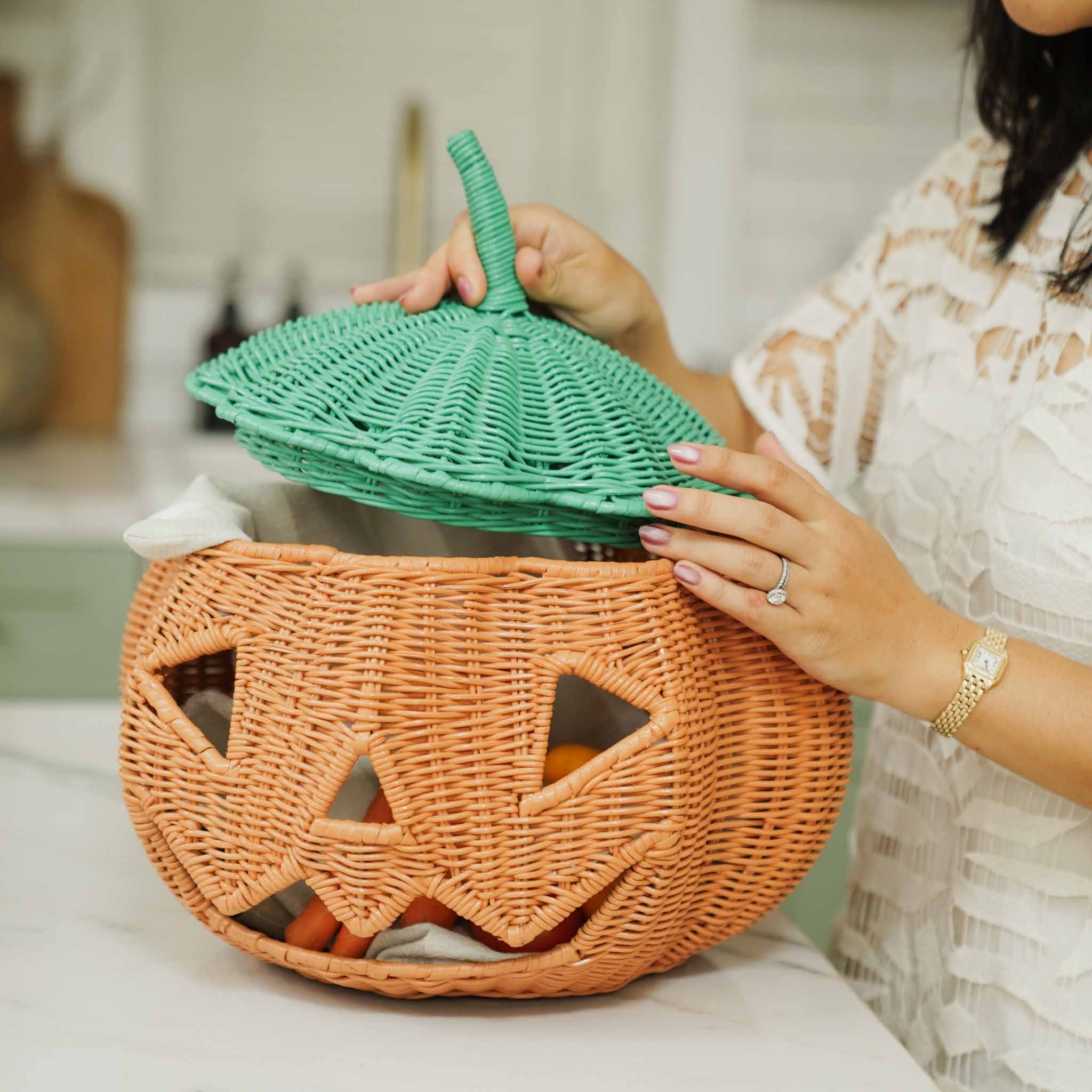 A woman opening the handcrafted Pumpkin Face Rattan Basket by MOMIJI, revealing treats inside and highlighting its spacious storage compartment and removable lid.