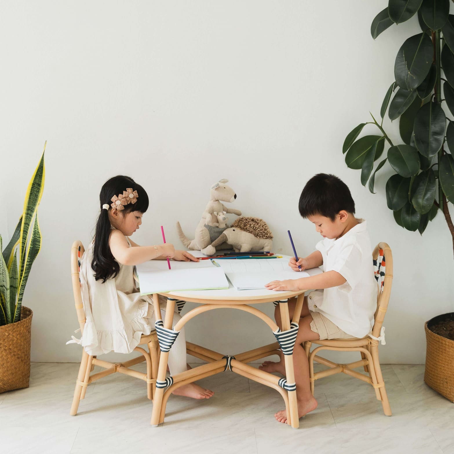 Two children sitting on handcrafted rattan and wicker Quentin Kids Chairs by MOMIJI at a small table, designed for shared learning and play.