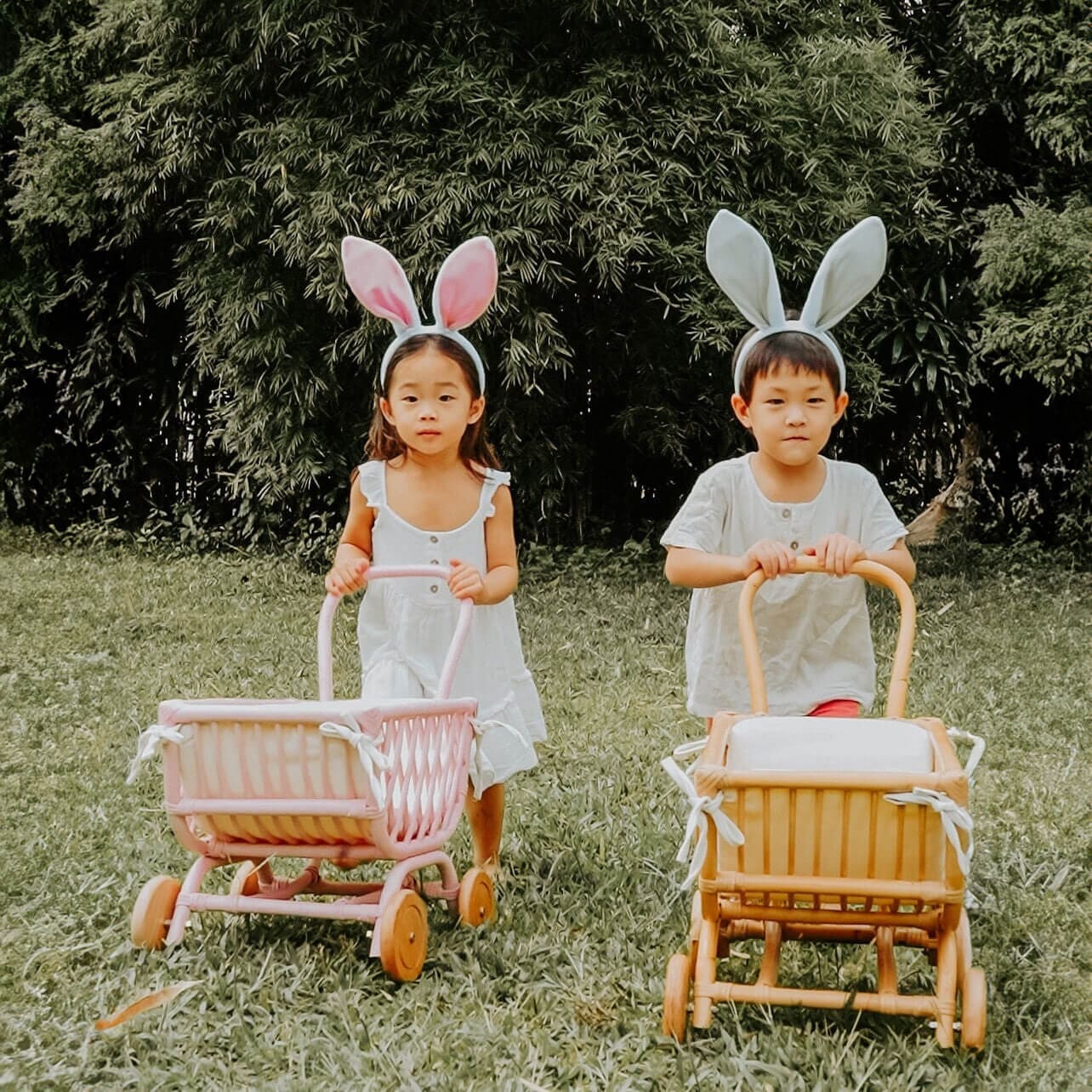 Two children wearing bunny ears playing with natural and pink color of the Rubble Toy Trolleys by MOMIJI outdoors.