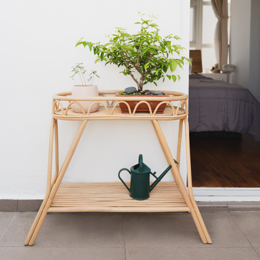 Sage Wicker Plant Stand by MOMIJI styled with potted plants on the top tray and a watering can on the lower shelf in a room setting.
