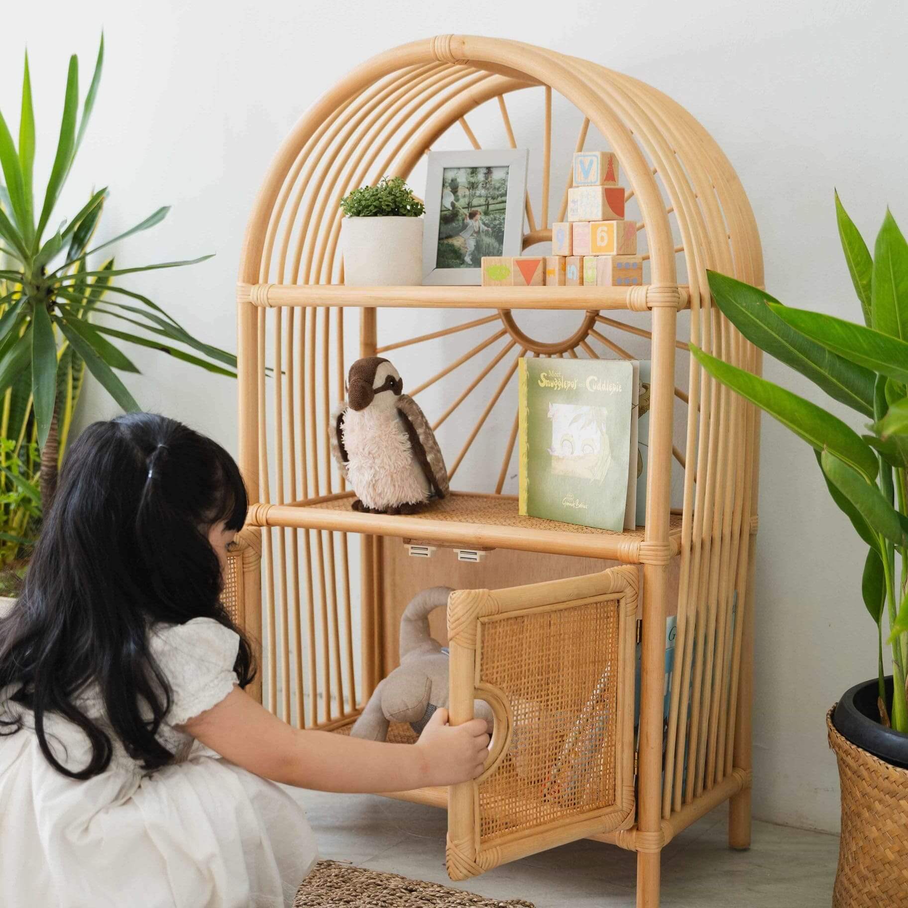 Child opening the cabinet door of the handcrafted rattan wicker Sunshine Arch Cabinet Shelf by MOMIJI in an indoor setting.
