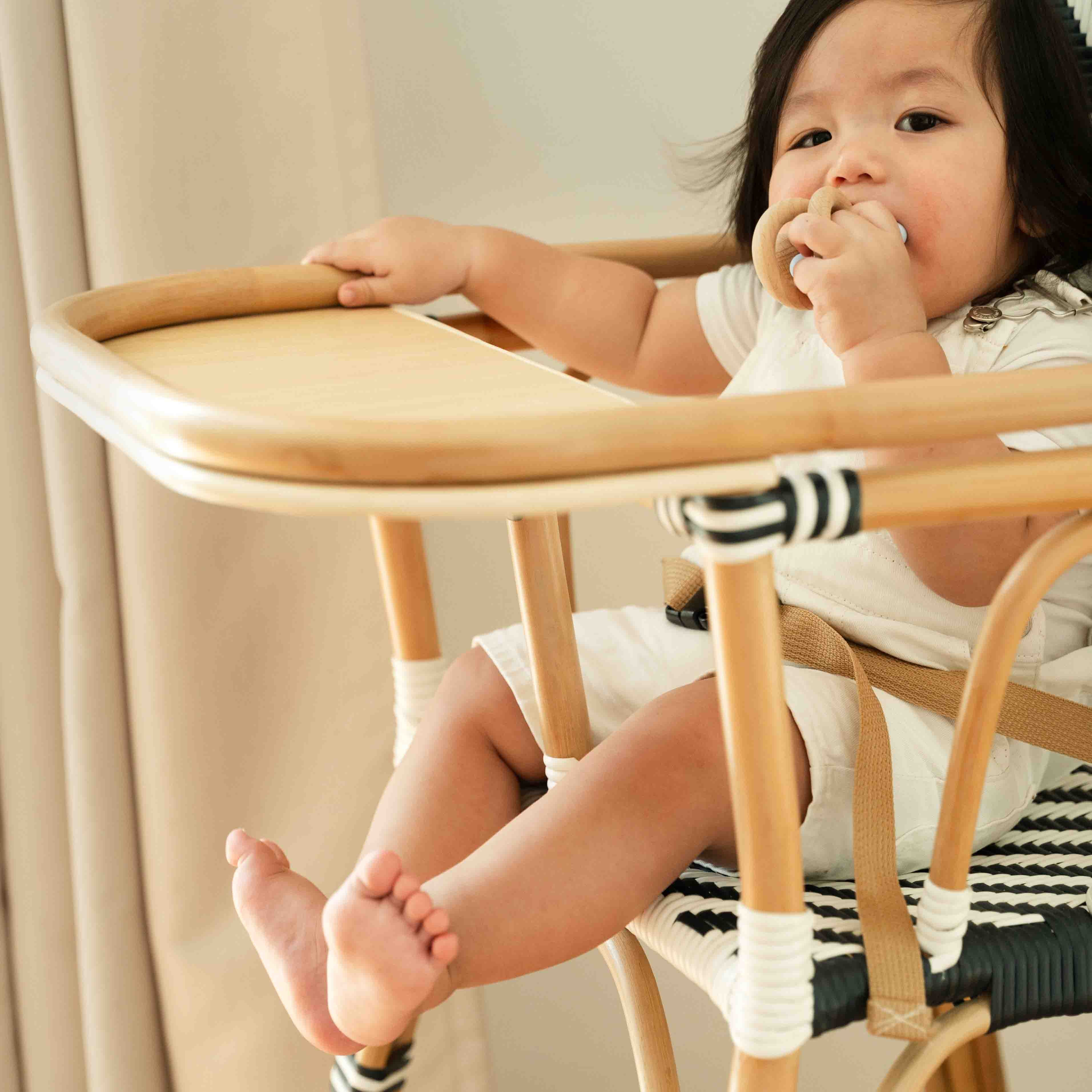 Child holding the armrest area of the Handcrafted rattan wicker Tumbuh Kids High Chair by MOMIJI during mealtime.