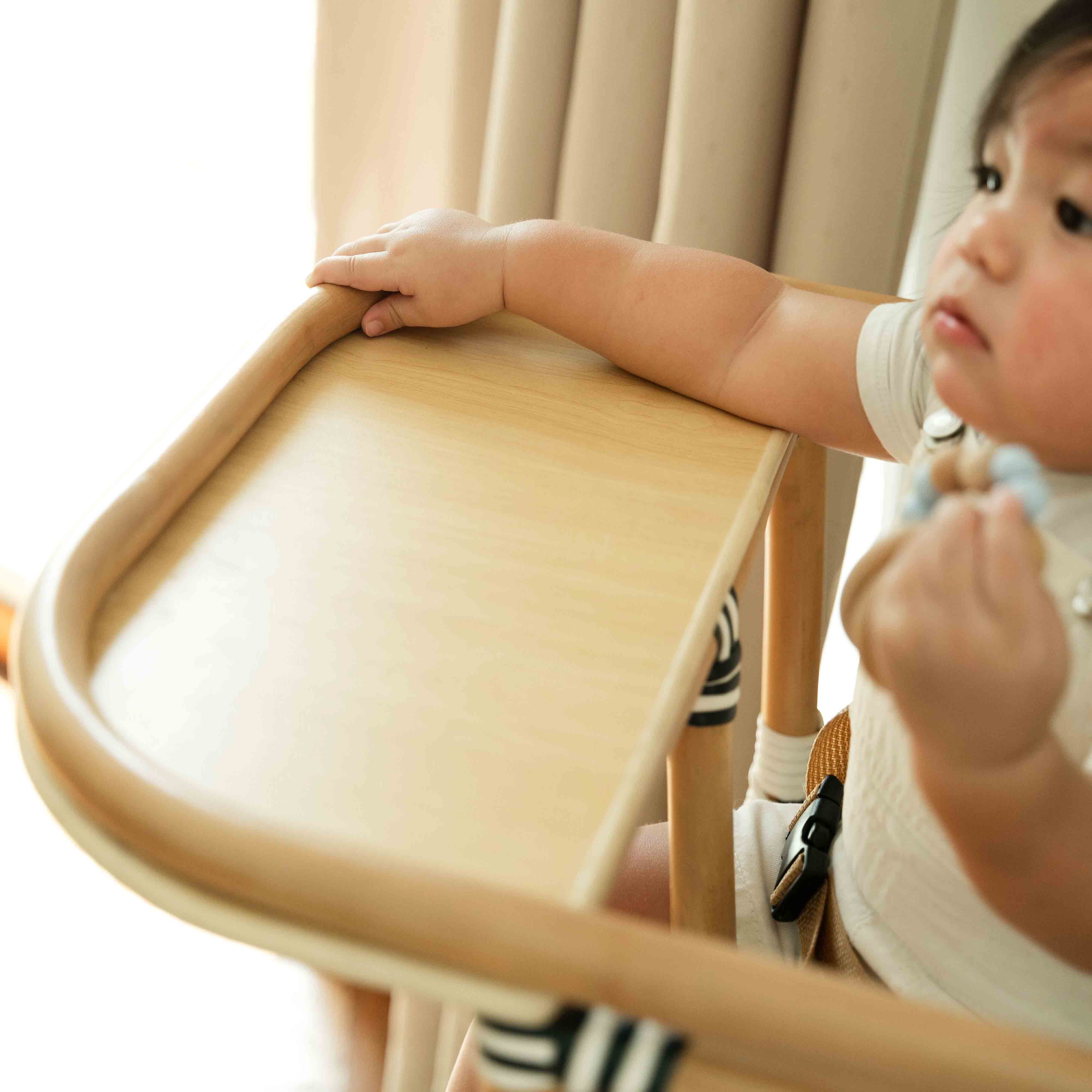 Close-up of a child holding the food tray of the Handcrafted rattan wicker Tumbuh Kids High Chair by MOMIJI.