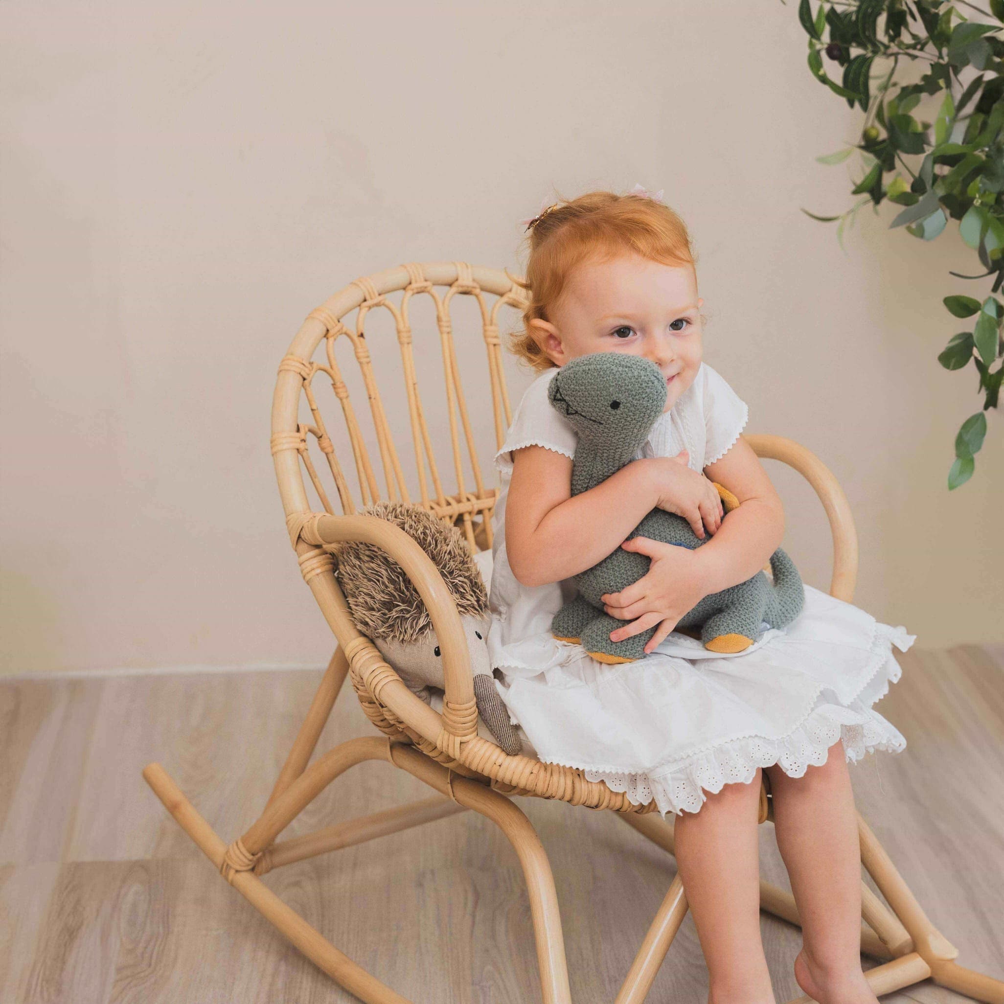 Happy child sitting on the Twinkle Kids Rocking Chair by MOMIJI hugging a doll with more toys beside.