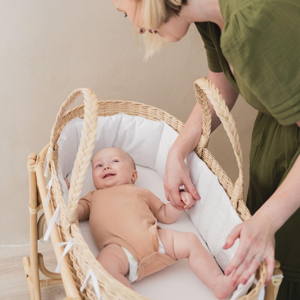 Top view of a baby lying in the handwoven rattan Vera Moses Basket by MOMIJI, laughing with the woman beside.