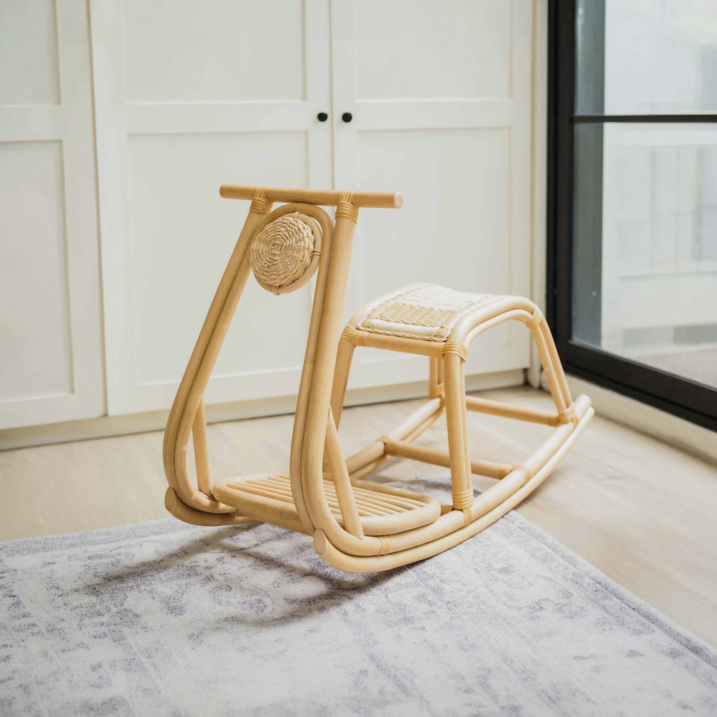 Handcrafted natural rattan Vespa Rocker by MOMIJI featuring a woven seat and decorative headlight-inspired rattan weaving, styled on a grey patterned rug in front of white panelled doors.