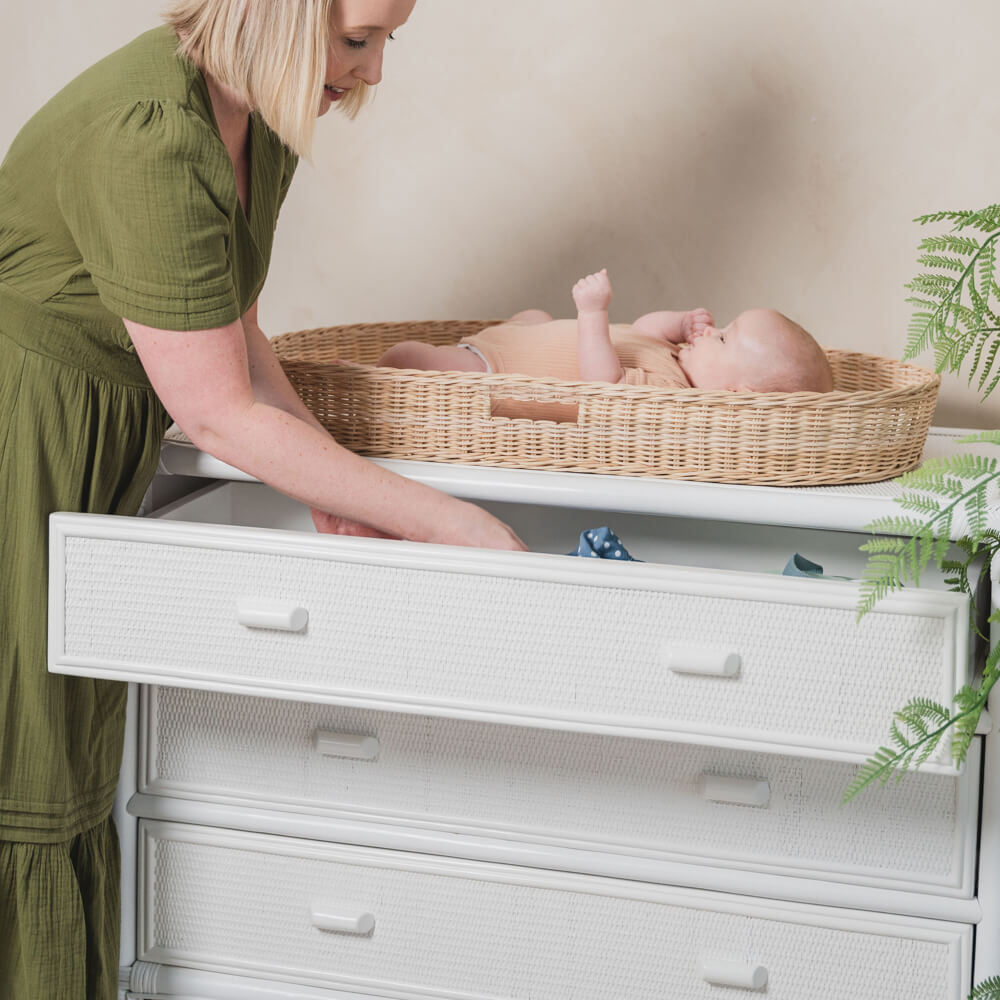 Woman reaching for baby clothes while interacting with a baby in the Xander Changing Basket by MOMIJI on a dresser.