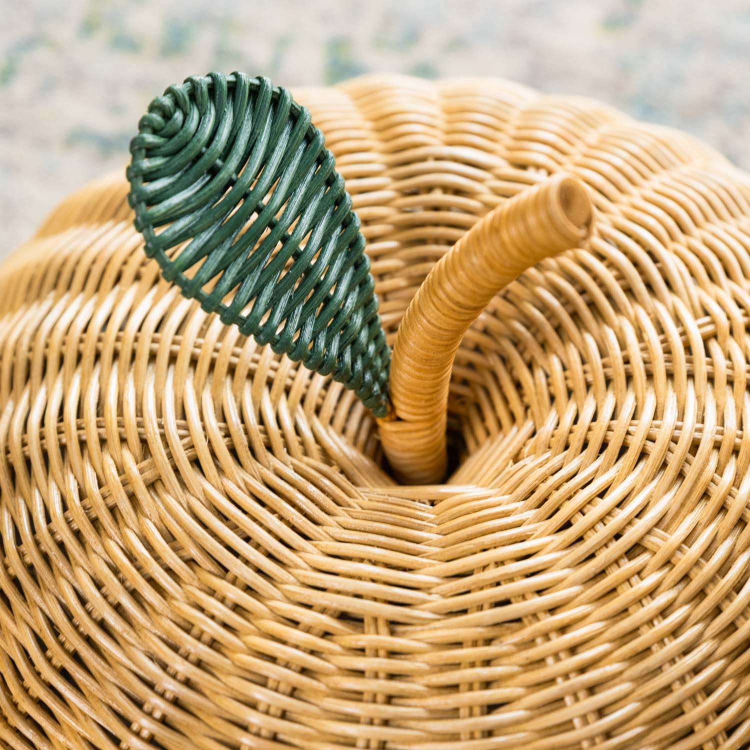 Close-up detail of the handcrafted natural rattan apple basket lid by MOMIJI, highlighting the green leaf and natural stem design.