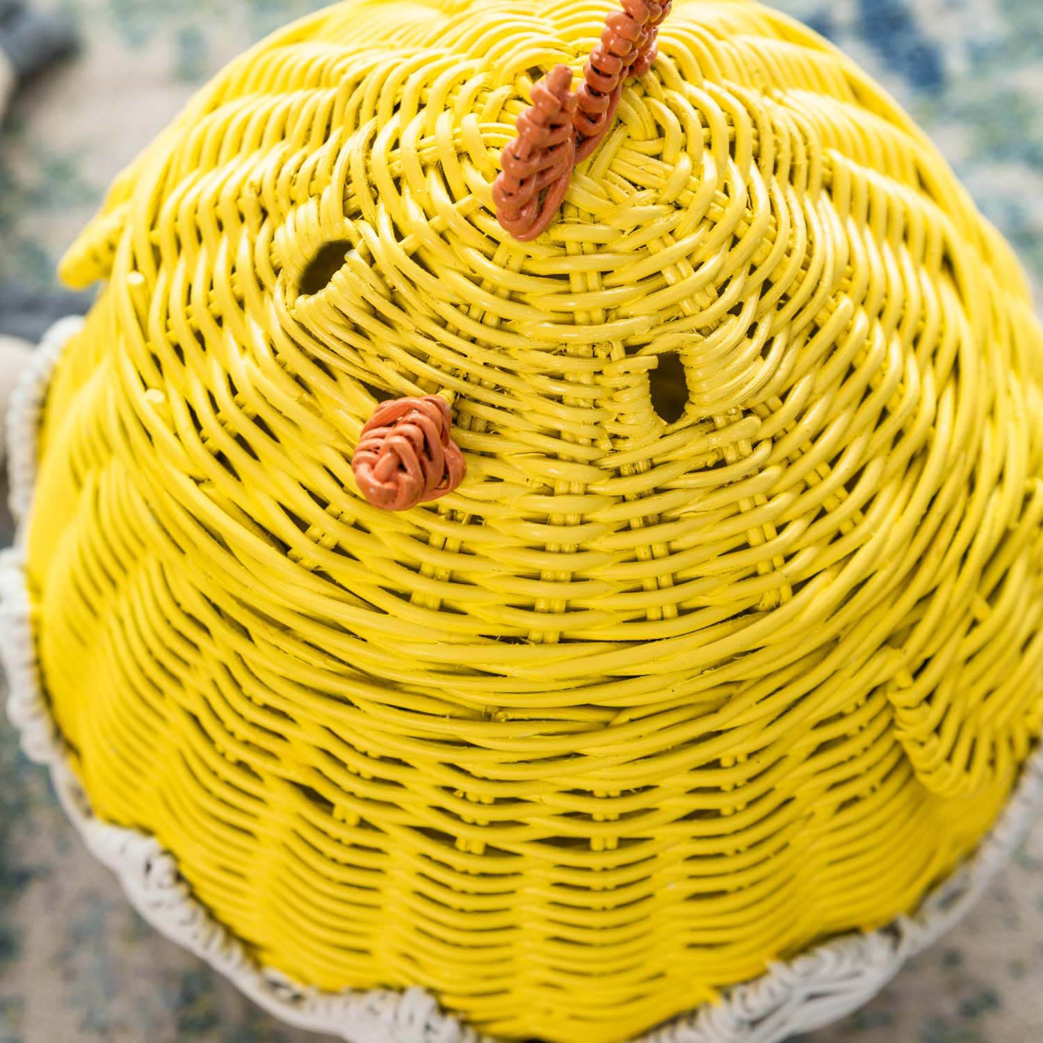 Close-up of the handcrafted yellow rattan and wicker chick basket lid by MOMIJI, showing rounded eyes, beak detail, and woven comb.