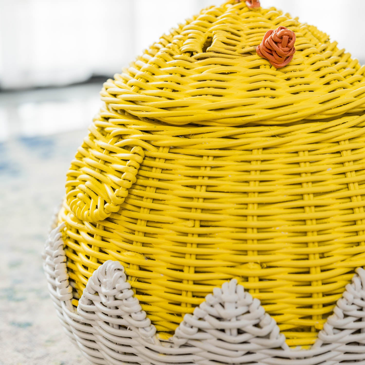 Close-up side view of a handcrafted yellow rattan wicker chick storage basket by MOMIJI, highlighting the woven wing detail and textured surface.