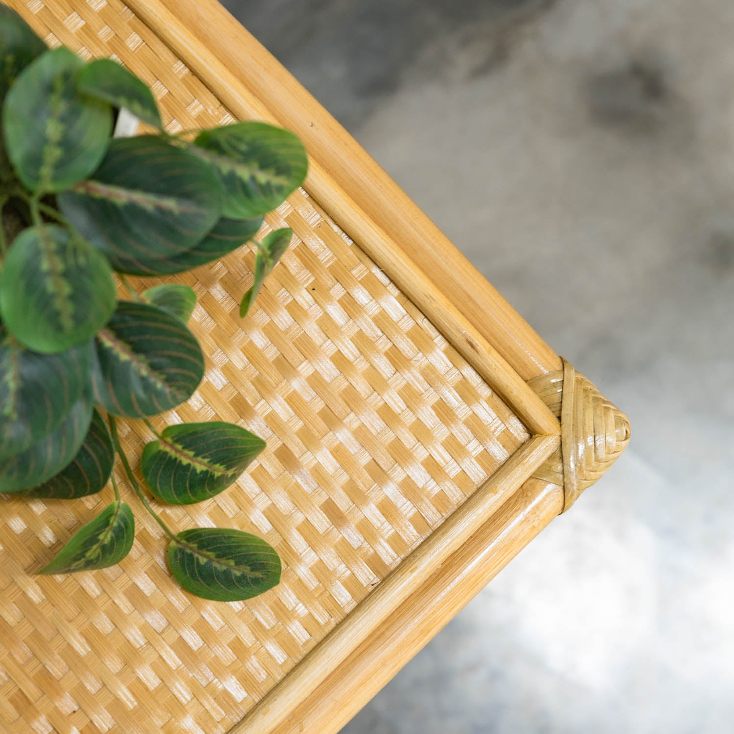 Top view close-up of a handcrafted wicker shelf with a plant, focusing on the woven rattan texture and the corner of the Graha Montessori storage shelf and basket by MOMIJI.