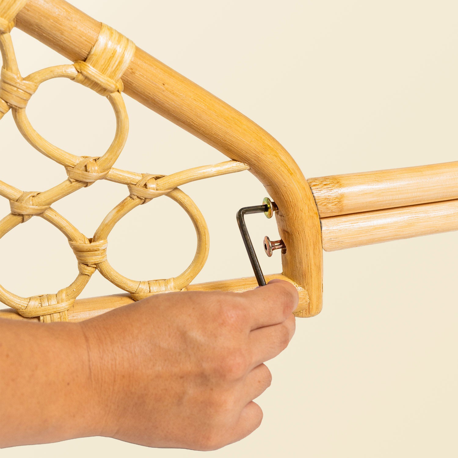 Hand holding a tool while assembling the handcrafted rattan wicker Layla Montessori floor bed by MOMIJI in beige natural rattan.