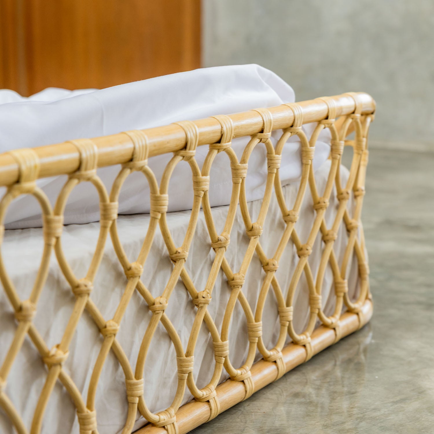 Close-up of the handcrafted Layla Montessori rattan floor bed by MOMIJI in natural beige with white bedding, highlighting the woven rattan details.