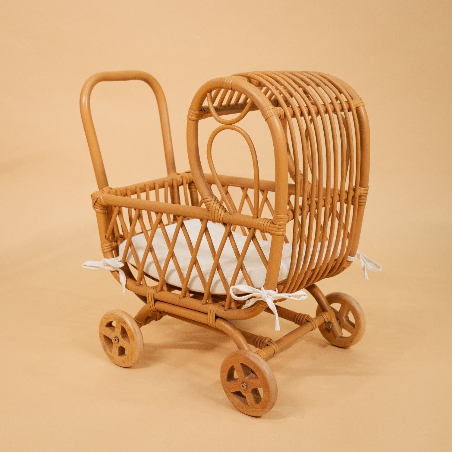 Side view of the handwoven rattan Layla Toy Stroller by MOMIJI in natural, with a white seat pad inside.