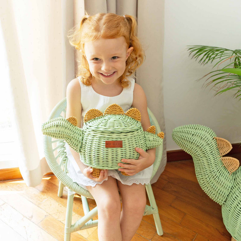 Child holding a Dinosaur Rattan Storage Basket Small by MOMIJI in a room with a plant in the corner.
