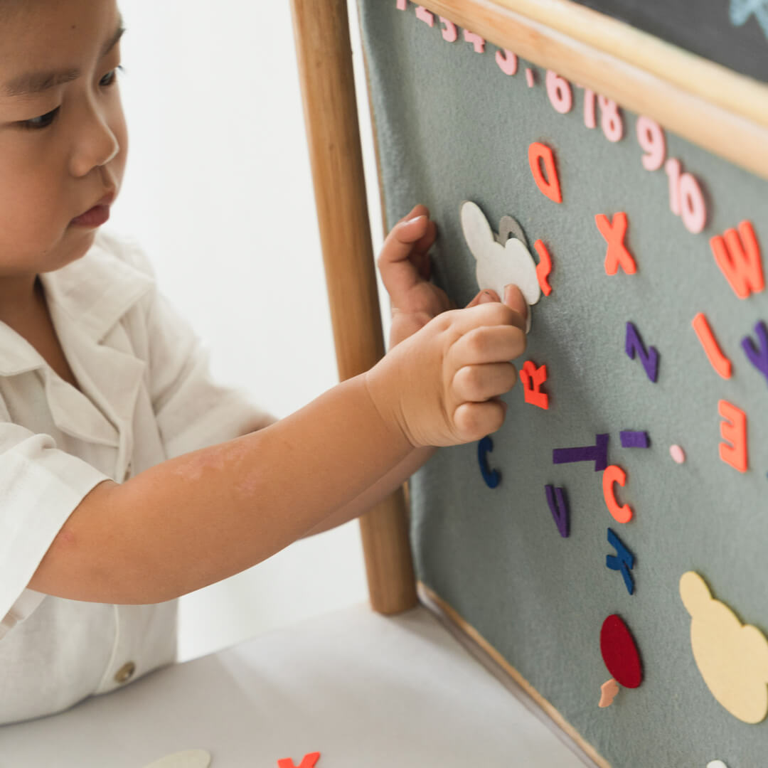 Child sticking letters and numbers on the learning board of the 3-in-1 furniture by MOMIJI.